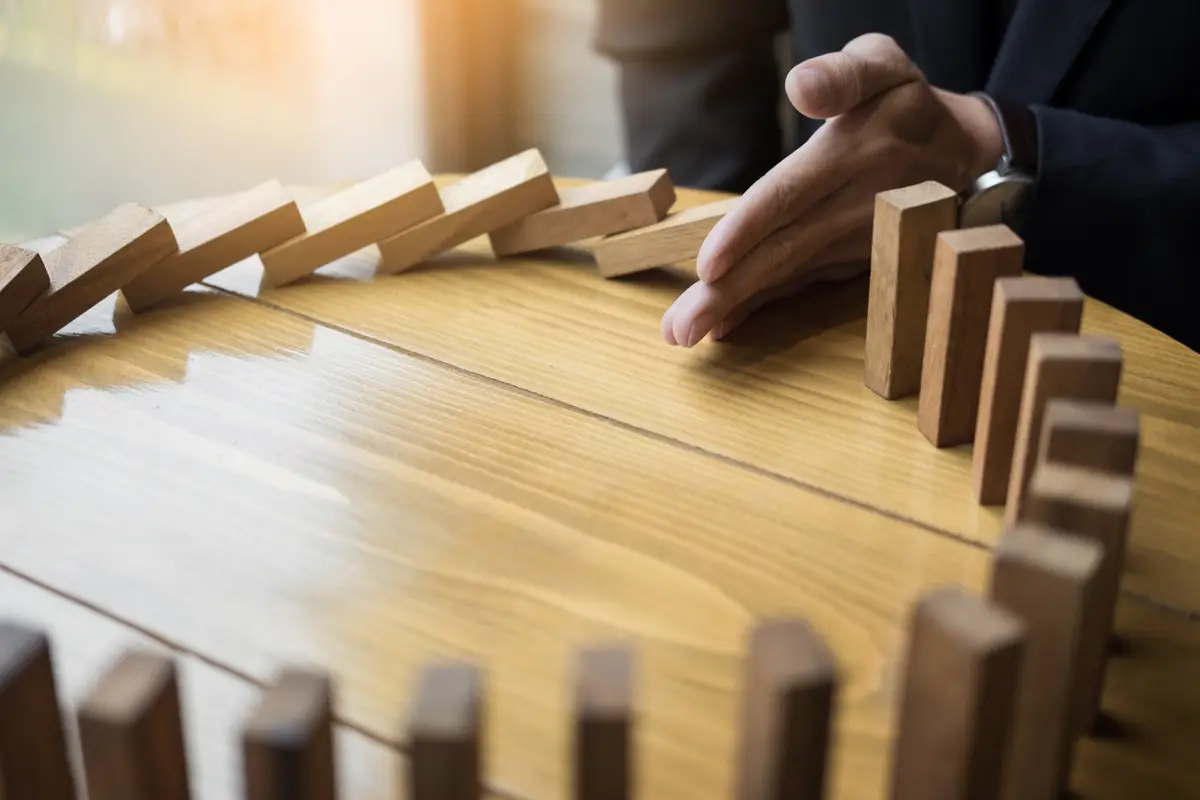 A steady hand halting a line of falling wooden blocks before they reach the standing ones, operational risk stopped before it spreads.