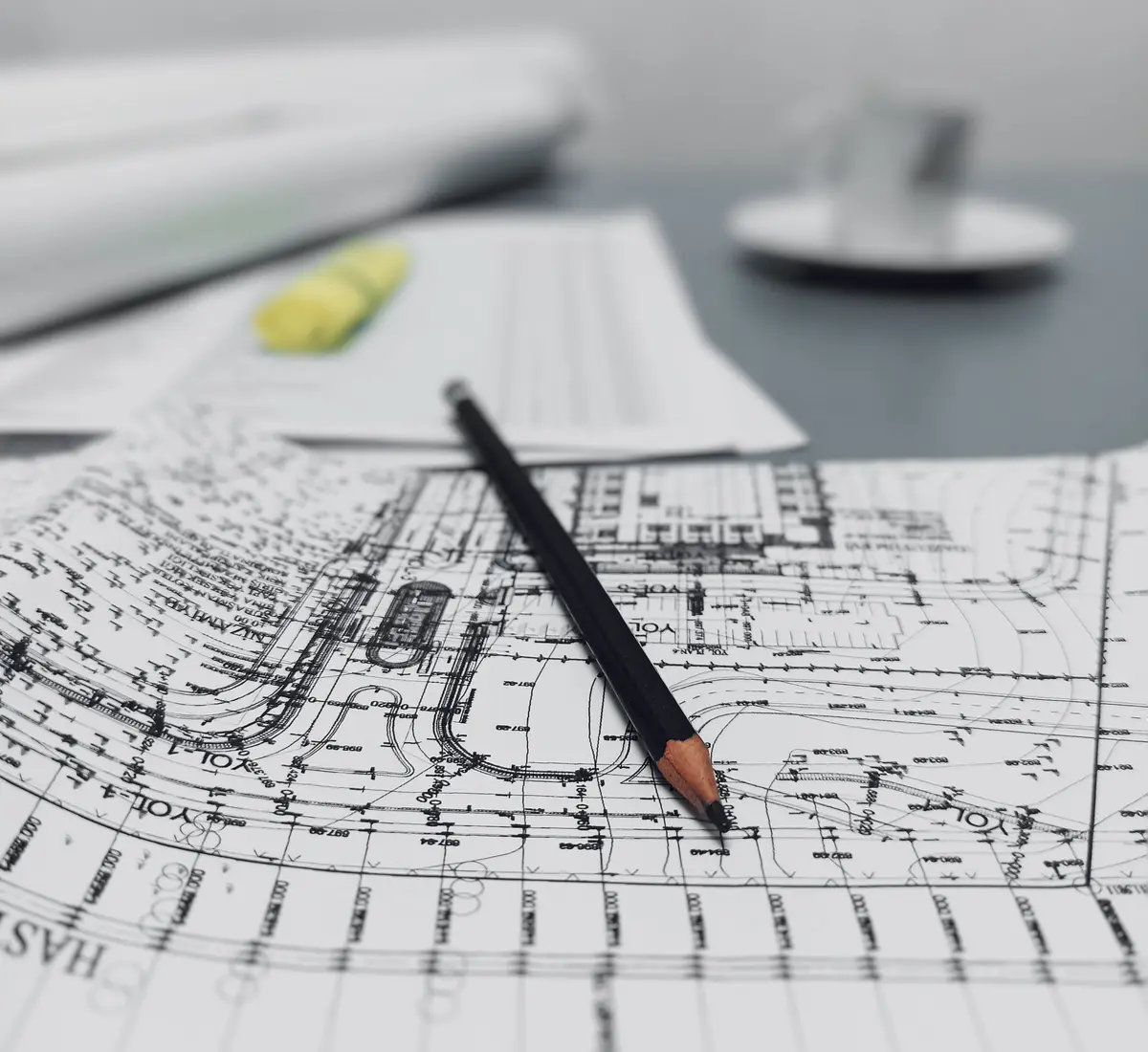 Architectural site plans with a sharpened pencil resting across them, a project drafted and detailed before a single decision is committed.
